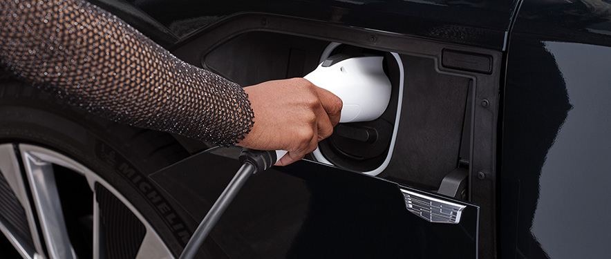 Woman's hand plugging a EV charger into a black Cadillac