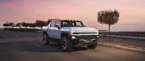 El nuevo vehículo eléctrico GMC HUMMER, en color blanco interestelar, en una carretera costera al atardecer.