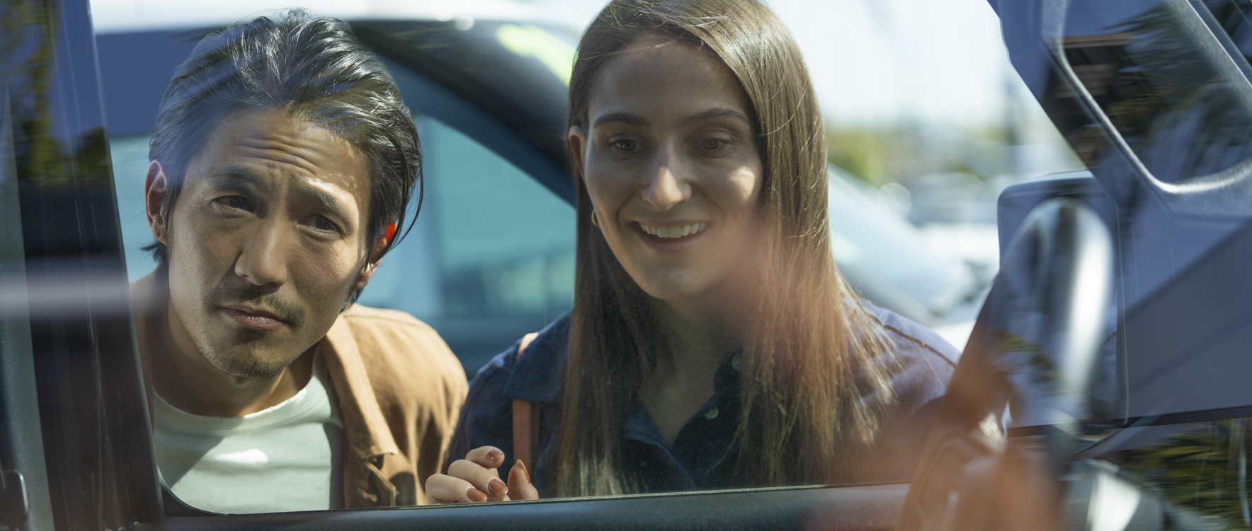 Happy woman with skeptical man looking through window of new car at dealership