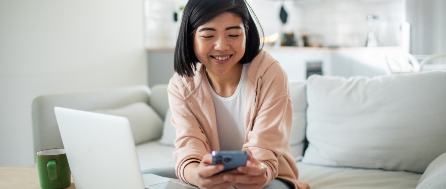 Mujer joven sonriente revisa el puntaje de crédito en su teléfono mientras solicita un financiamiento de automóvil.