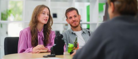 Young couple asking a car salesman questions about auto financing at a dealership.